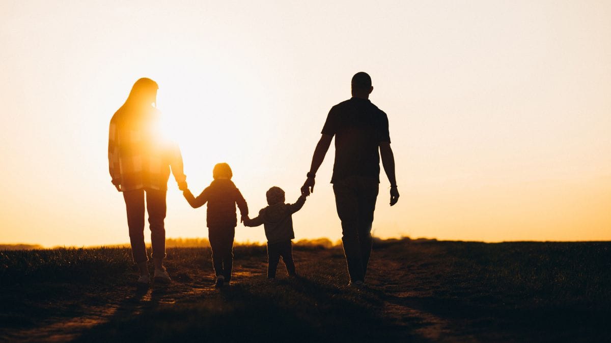 Família de mãos dadas caminhando ao pôr do sol, representando a vocação cristã e o chamado de Deus.