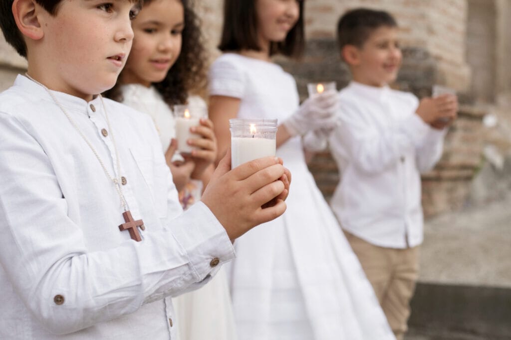 Crianças vestidas de branco segurando velas durante a celebração da Primeira Eucaristia.